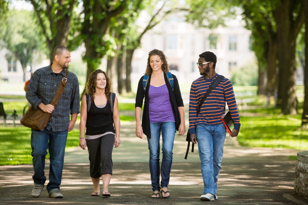 Four students, two men and two women, walk together across their college campus.