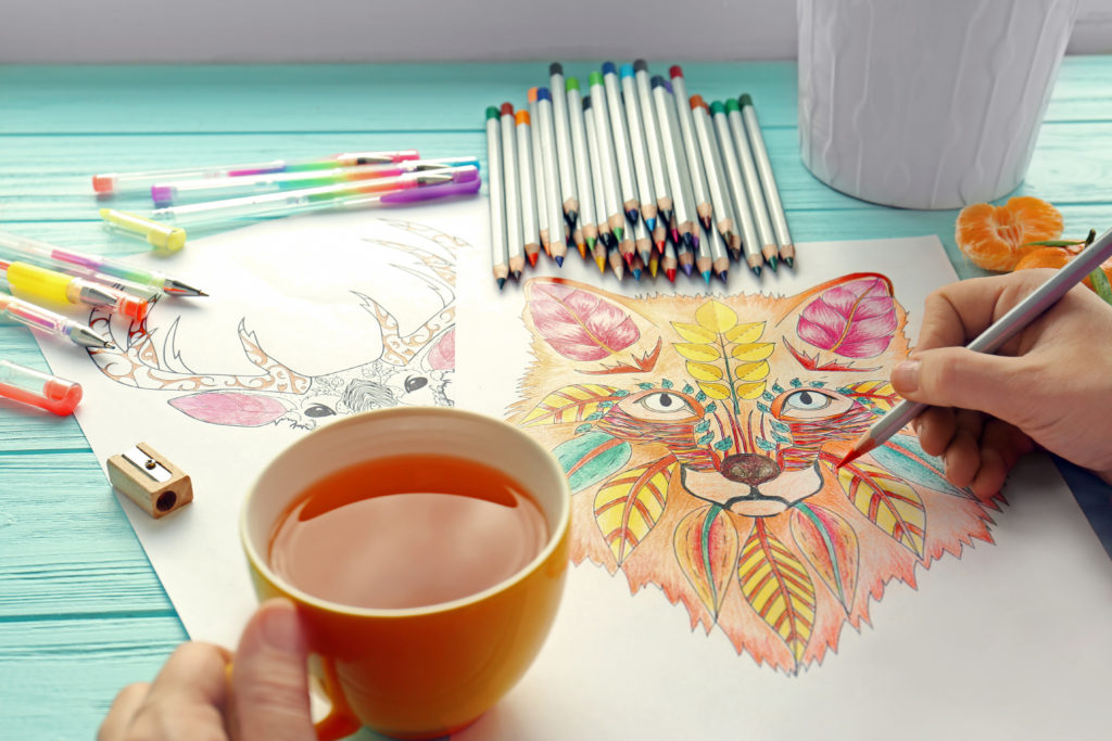 Self-care for tough times. Closeup of woman sitting at table with coloring book, colored pencils, and a cup of hot tea.