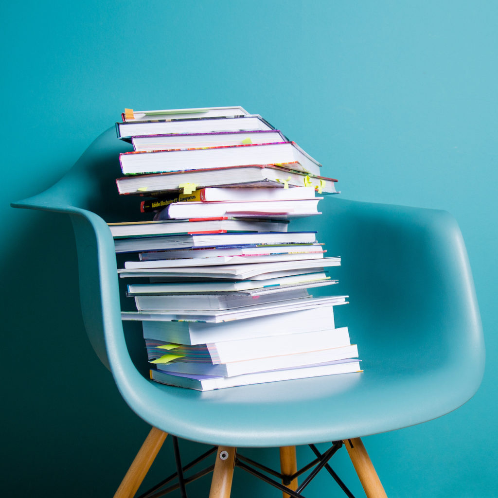A large stack of books in a aqua colored chair